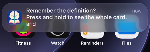 A Miji notification over the iPhone home screen. It says Remember the definition? Press and hold to see the whole card. Under that is the word arid.